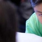 A young student writes with a pencil in a classroom at a desk